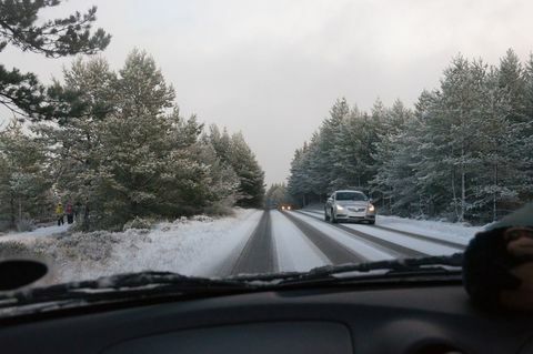 Auto sõidab lumega kaetud teel puude vahel