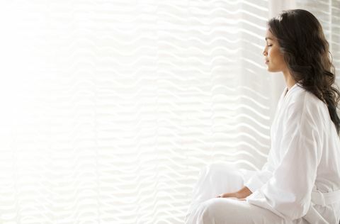 Rahulik naine hommikumantlis, kes mediteerib päikselisel aknal
